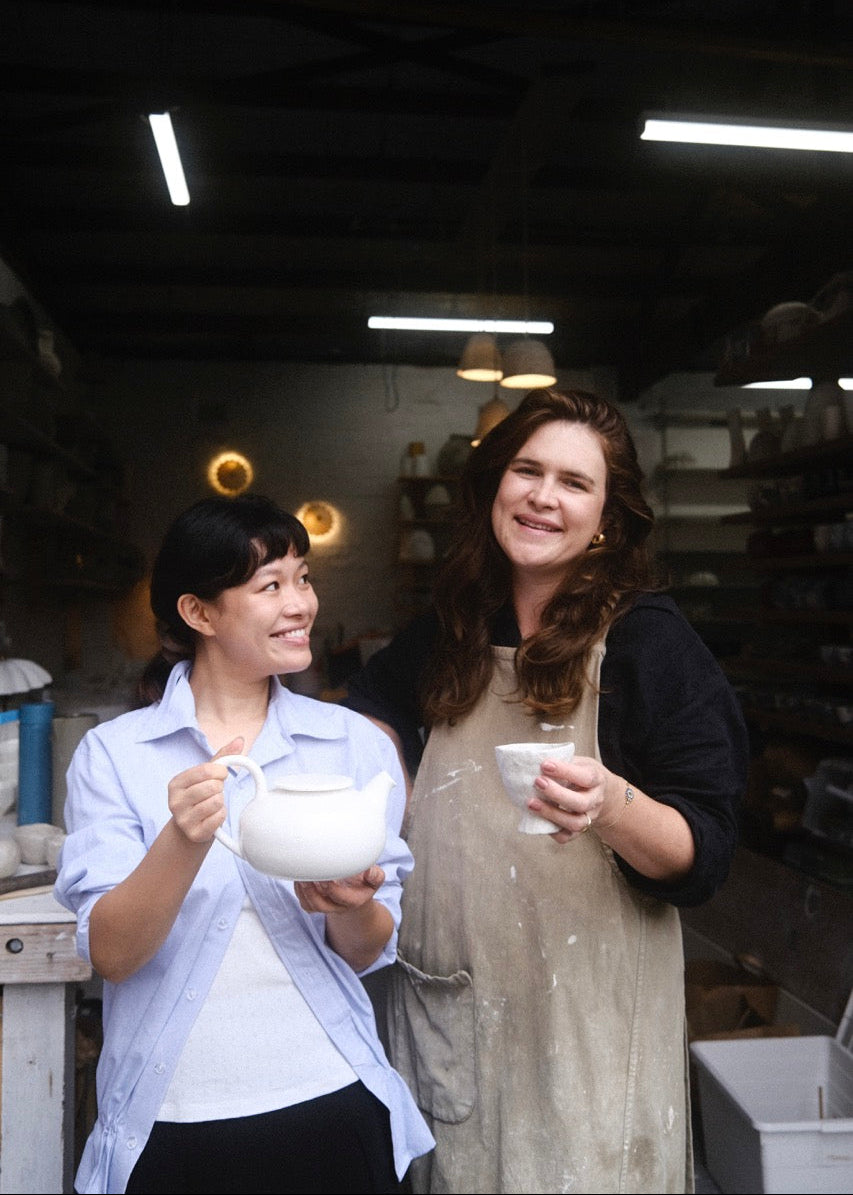 Two women in a workshop holding ceramic items.